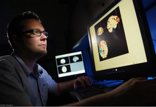 Forrás: index.hu / Colorado Egyetem hallgatója, nézi az agyról készített fMRI felvételeket, amelyek a kongitív viselkedést szabályozó területeket mutatja pirossal kiemelve / Fotó: Glenn Asakawa